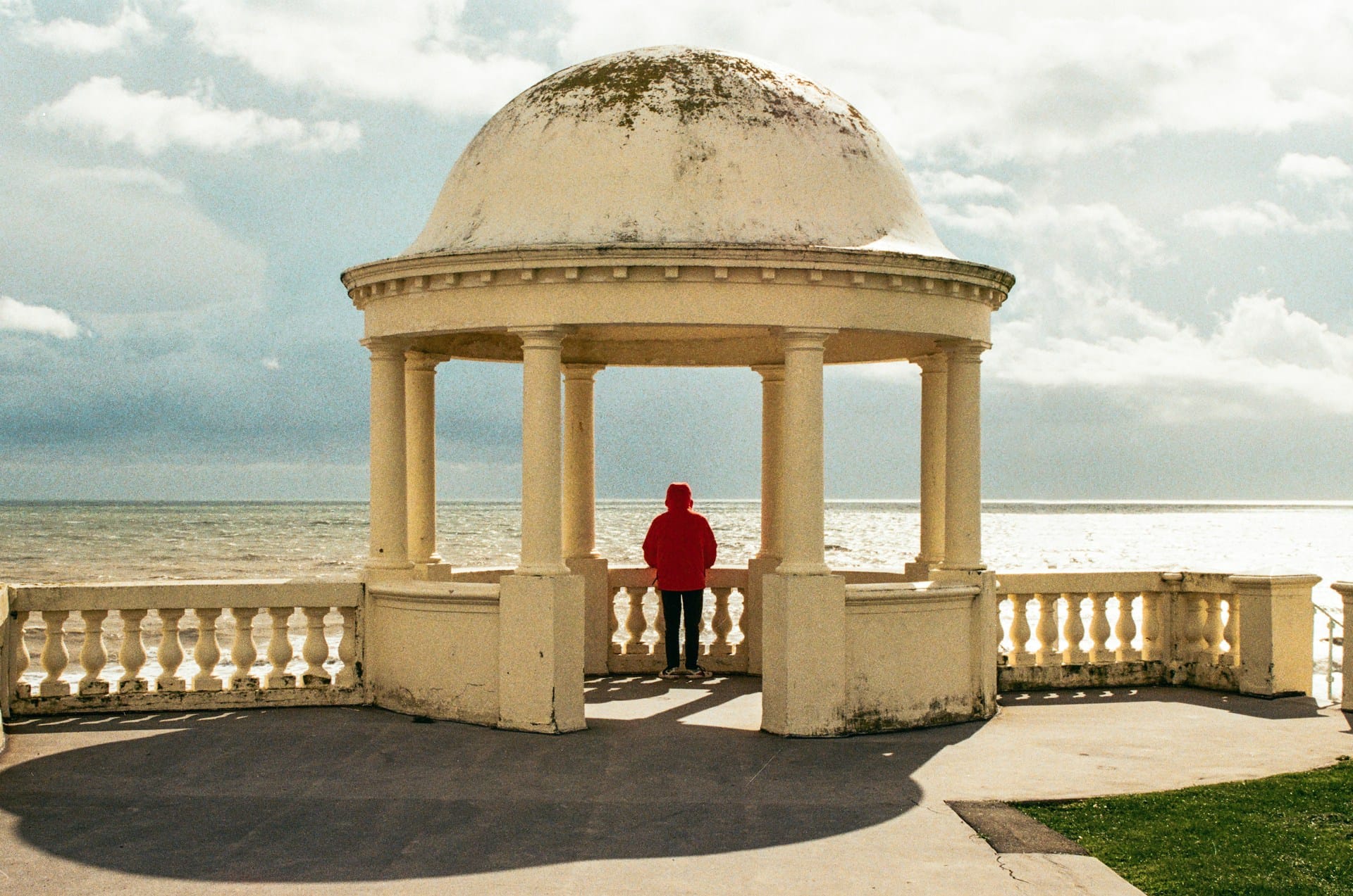 A person wearing a red hoodie under a small gazebo overlooking the ocean