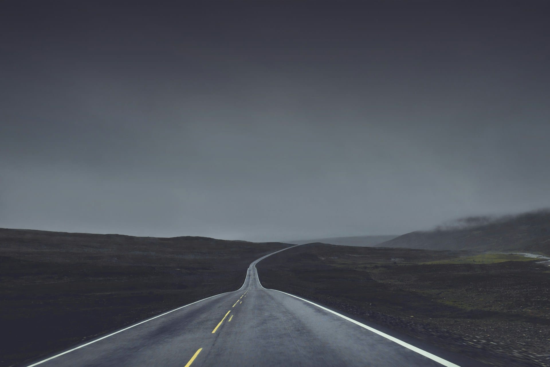 A two lane road winding underneath a dark and cloudy sky